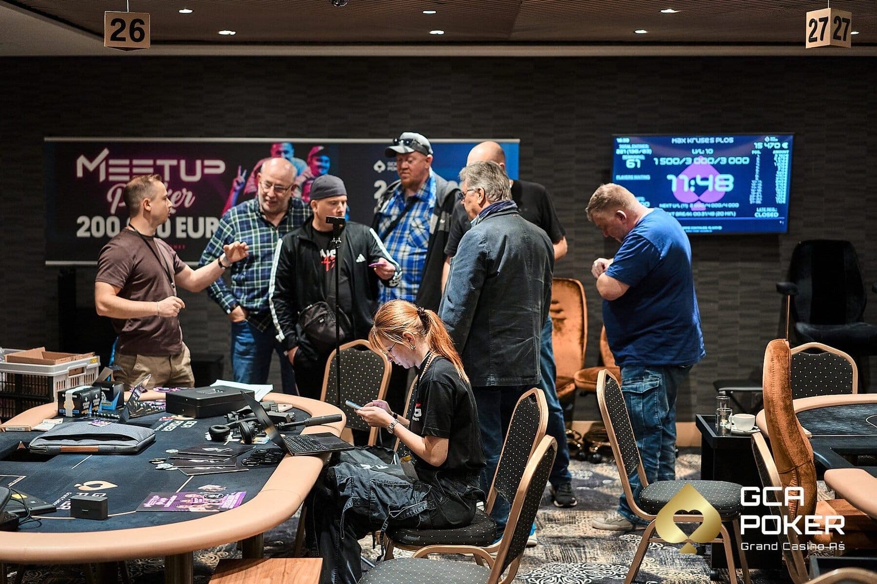 Angi arbeitet beim Meetup-Poker-Event am Laptop und Handy, im Hintergrund Spieler und Turnieranzeige